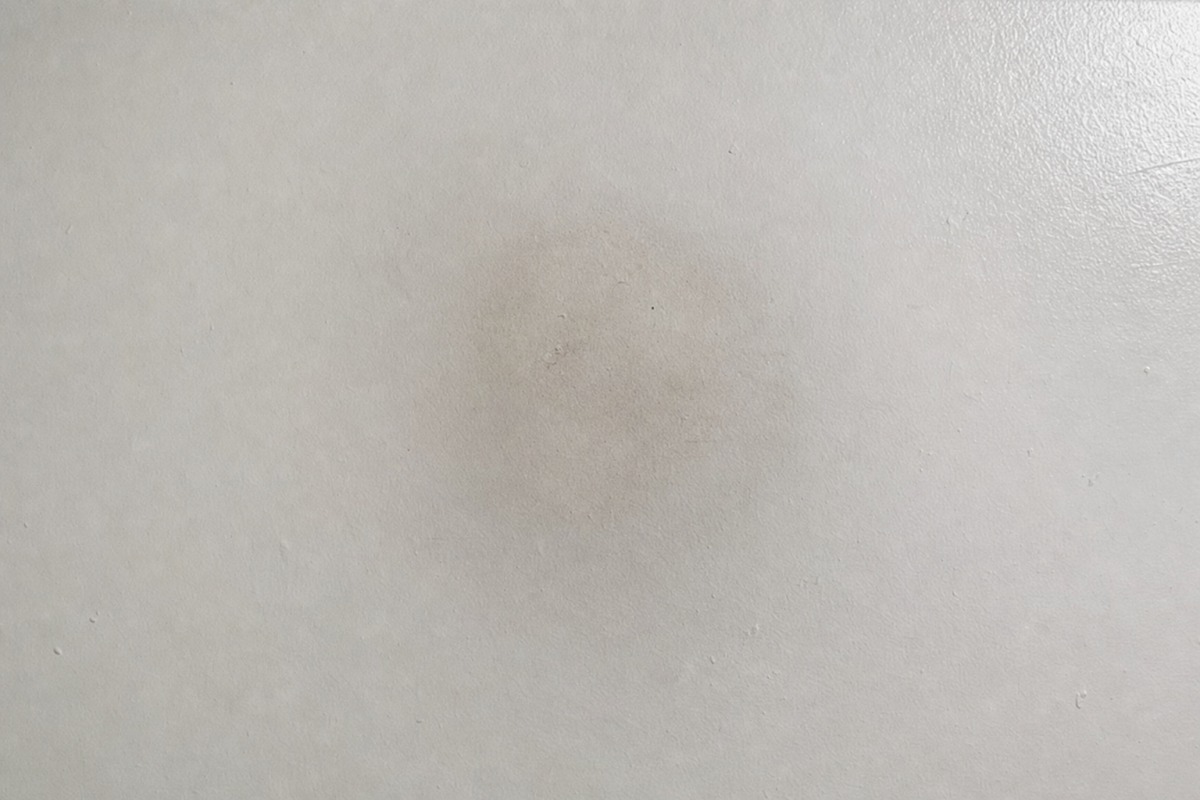 Maiga pelēka kvēpu ēna uz balta griestu laukuma virs vietas, kur stāvēja parafīna svece